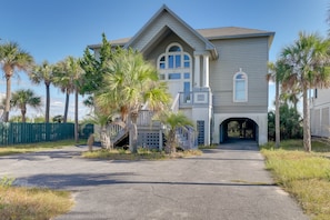 A two-story house with a covered driveway, palm trees, and a green fence. - Spacious Isle of Palms Home w/ Ocean Views! (Isle of Palms)