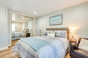 A bedroom with a large bed, a bedside table with a lamp, a mirror, and a painting on the wall.