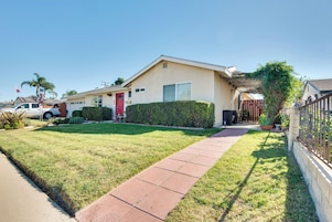 A single-story house with a red door, a front yard with a paved walkway, and a small garden area.