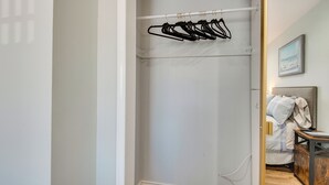 Un dressing avec un mur blanc, un plancher en bois et une tringle en métal avec des cintres noirs.