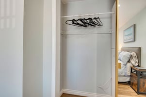 A walk-in closet with a white wall, a wooden floor, and a metal rod with black hangers.