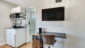 Une cuisine compacte équipée d’un four à micro-ondes encastré, d’une machine à café et d’un petit réfrigérateur. Un téléviseur est fixé au mur, au-dessus d’un bureau avec une chaise.