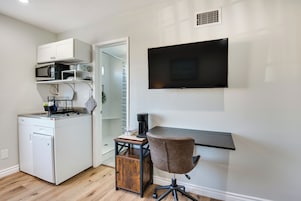 A compact kitchen with a built-in microwave, coffee maker, and a small refrigerator. A TV is mounted on the wall above a desk with a chair.
