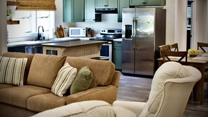 Une cuisine moderne avec des meubles de couleur verte, un réfrigérateur en acier inoxydable et un coin repas comprenant une table et des chaises en bois.