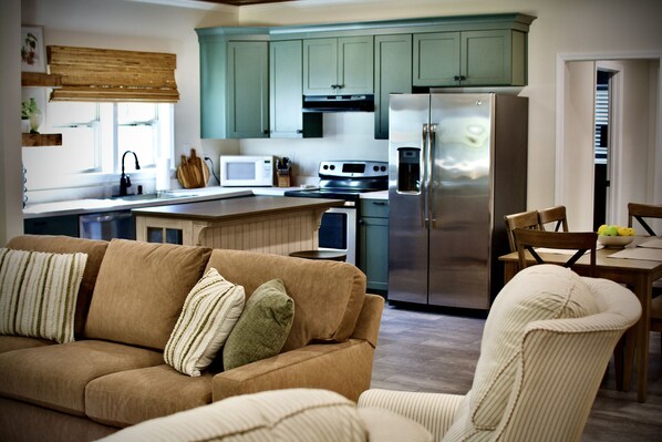 Una cocina moderna con armarios verdes, un refrigerador de acero inoxidable y un comedor con mesa y sillas de madera.