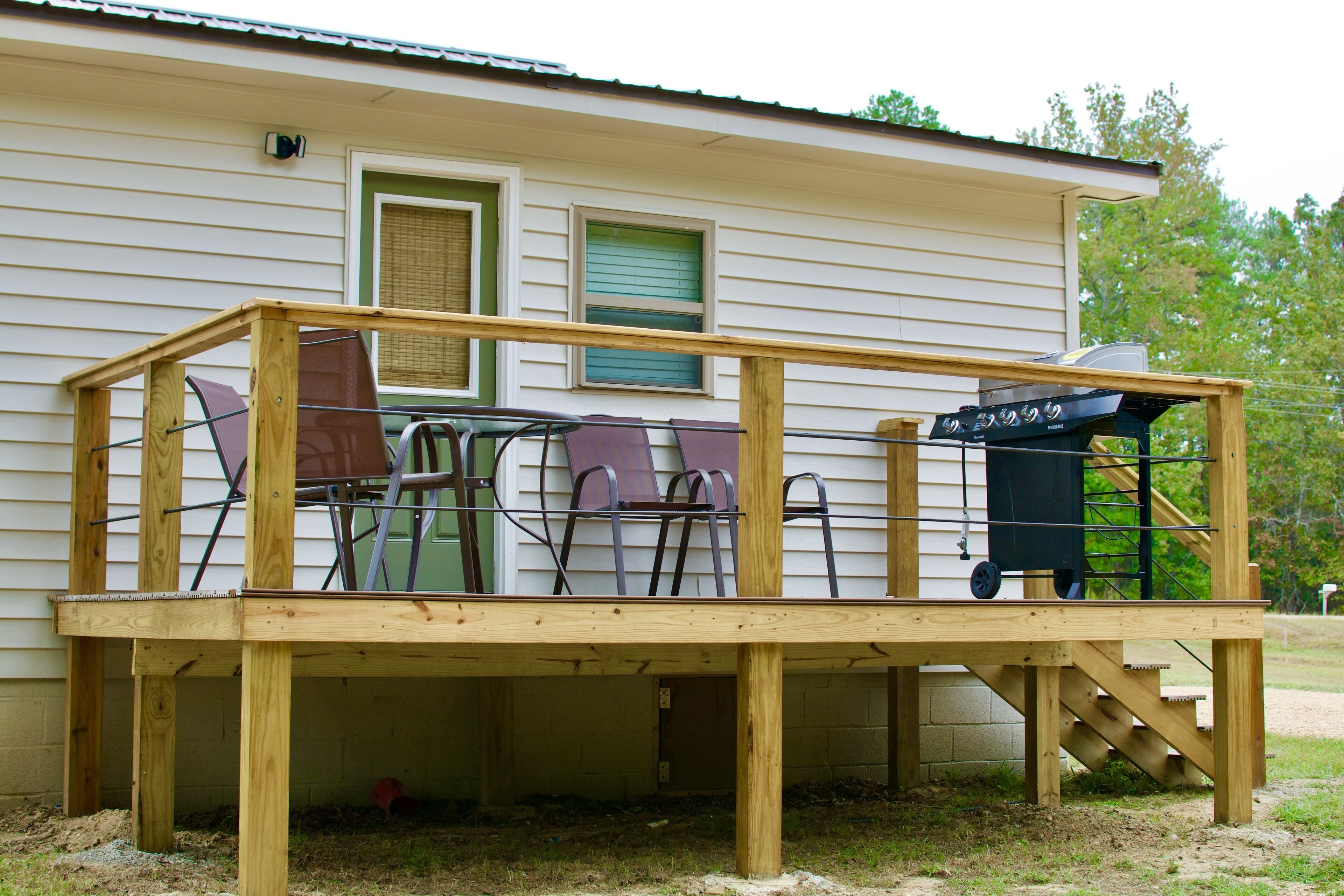 Une terrasse en bois avec une table et des chaises, un barbecue et une fenêtre avec des stores.