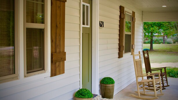 Une véranda avec une chaise berçante en bois, une porte et une boîte aux lettres.