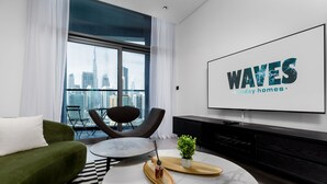 Een moderne woonkamer met een groene bank, een ronde salontafel, een aan de muur bevestigde televisie en een stadszicht door grote ramen.