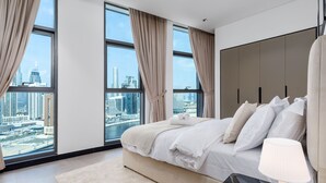Een moderne hotelkamer met een groot bed, een nachtkastje, een lamp en uitzicht op de stadshemel door grote ramen.
