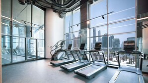 Een moderne sportschool met loopbanden langs een groot raam met uitzicht op een stadsbeeld.
