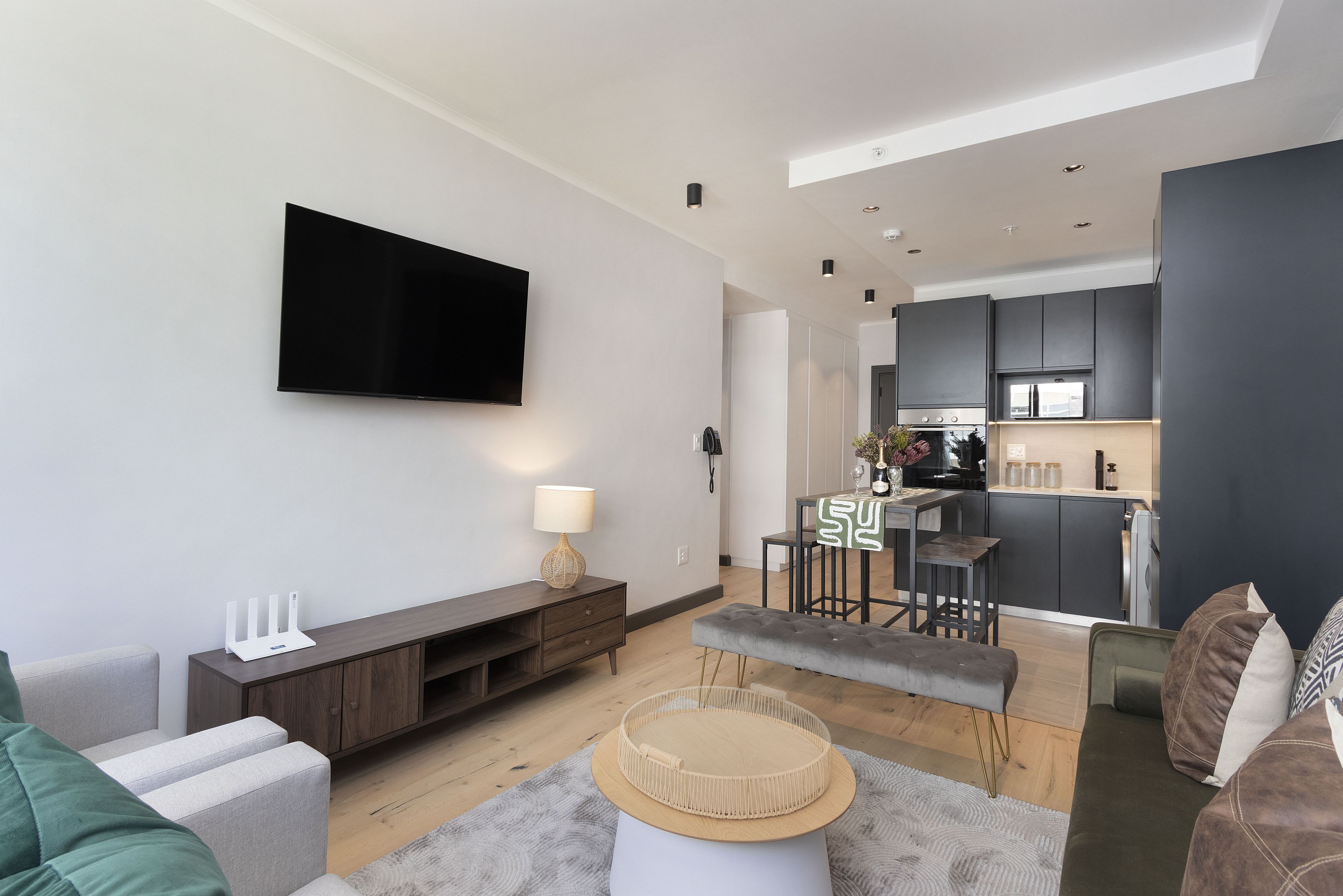 A modern living room with a flat-screen TV, a wooden entertainment unit, a grey sofa, and a small round table.
