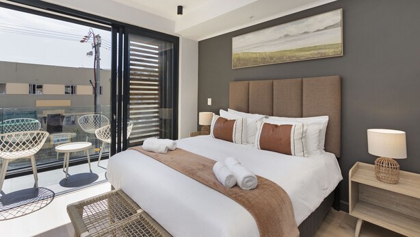 A modern hotel room with a large bed, a balcony with seating, and a view of the cityscape. - Portswood 103 (Cape Town)