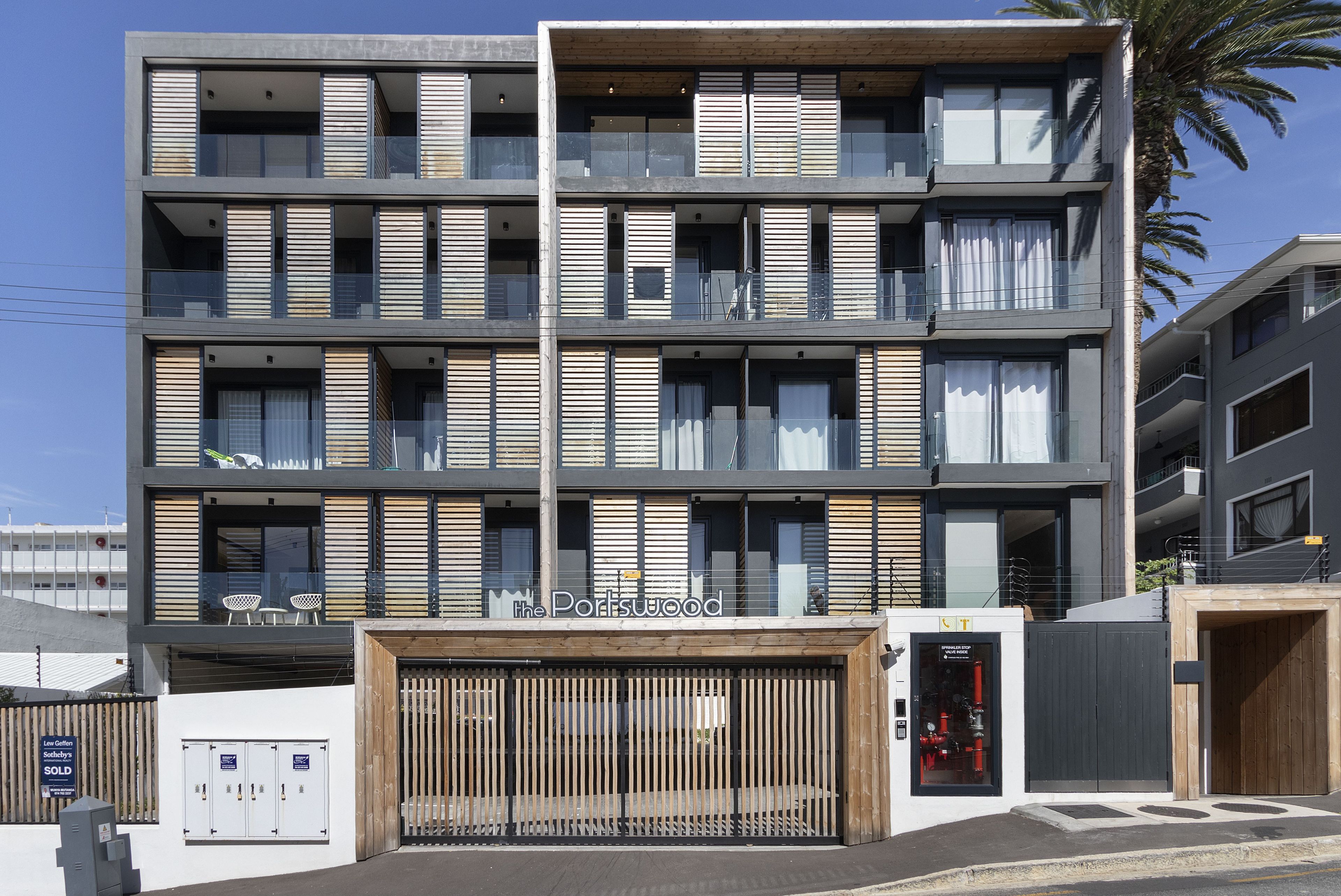 Un immeuble à plusieurs étages doté de balcons, d’un portail en bois et d’une enseigne sur laquelle on peut lire « The Portwood ».