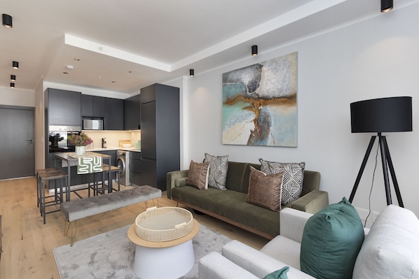 A modern living room with a sofa, a coffee table, and a dining area with stools.