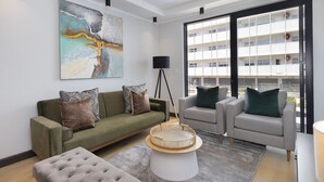 A modern living room with a sofa, armchairs, a coffee table, and a large window with a view of a building. - Portswood 103 (Cape Town)