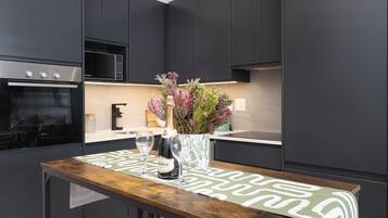 Una cocina moderna con armarios oscuros, un horno Bosch, un microondas, una mesa de madera con un mantel corrido de diseño verde y blanco, y un jarrón con flores.
