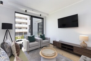 A modern living room with a sofa, two armchairs, a TV, and a lamp. - Portswood 103 (Cape Town)