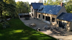 Une maison à deux étages dotée d’un patio couvert, d’un espace de jeux et d’une cour en gravier aménagée avec du mobilier d’extérieur.