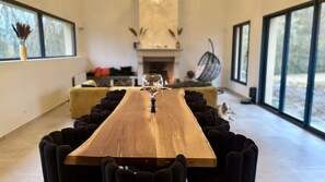 Une longue table à manger en bois, avec des chaises à revêtement noir, un verre de vin et une cheminée en arrière-plan.