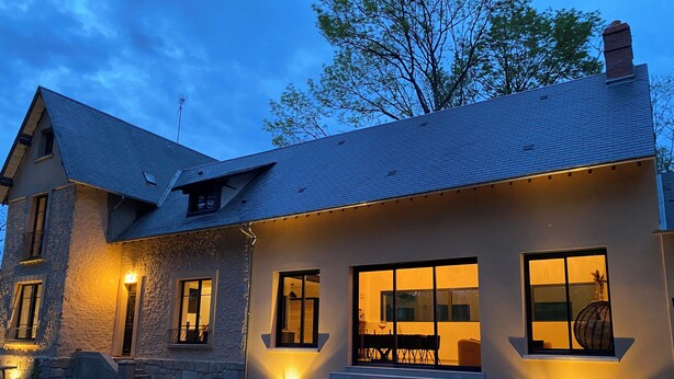 Una casa de piedra con techo inclinado, ventanas grandes y una entrada bien iluminada.