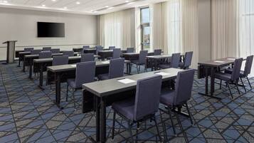 Un salón de conferencias con varias mesas y sillas, una pantalla de proyector y un atril.