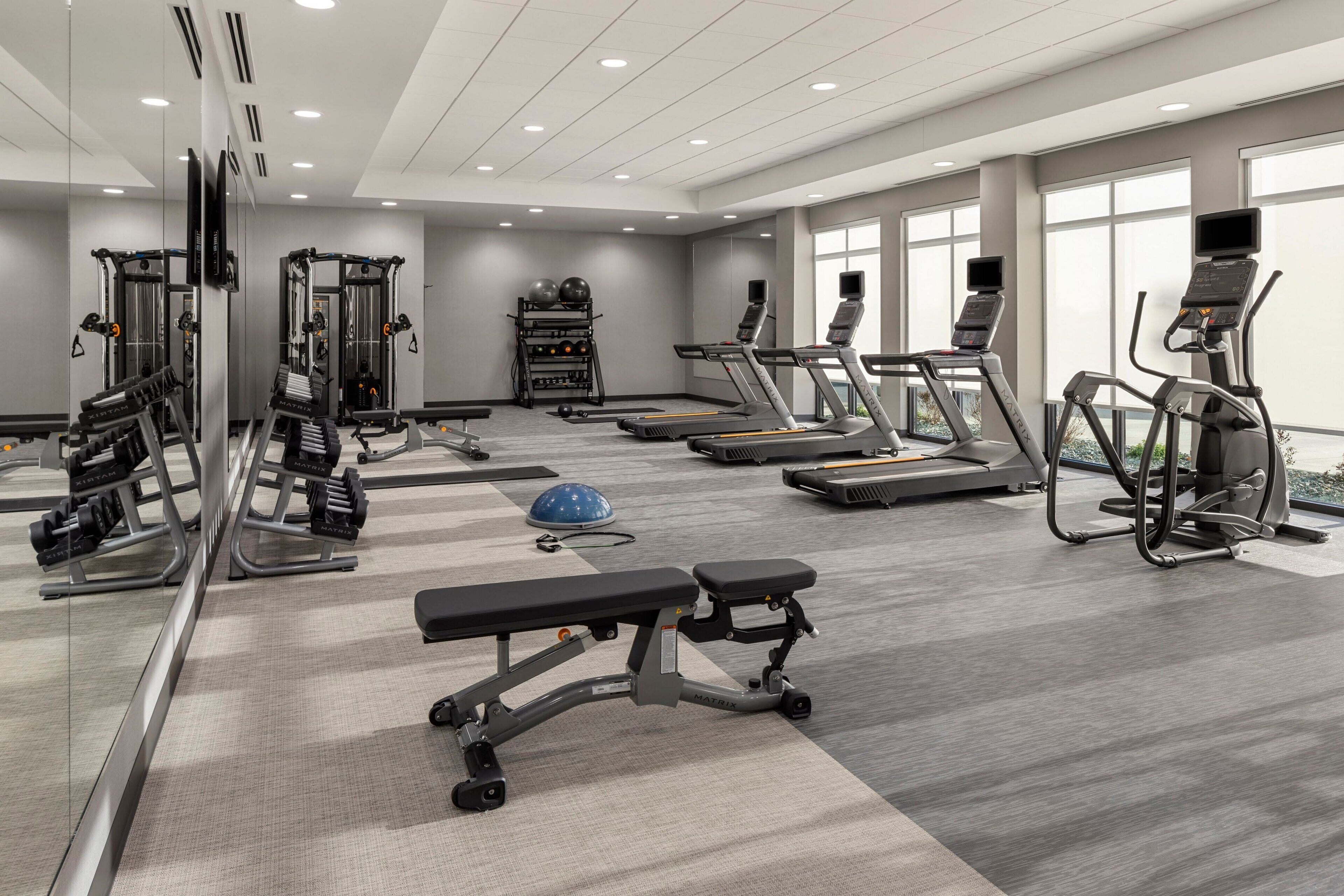 Een moderne sportschool met diverse fitnessapparaten, waaronder loopbanden, krachttoestellen en een bank.