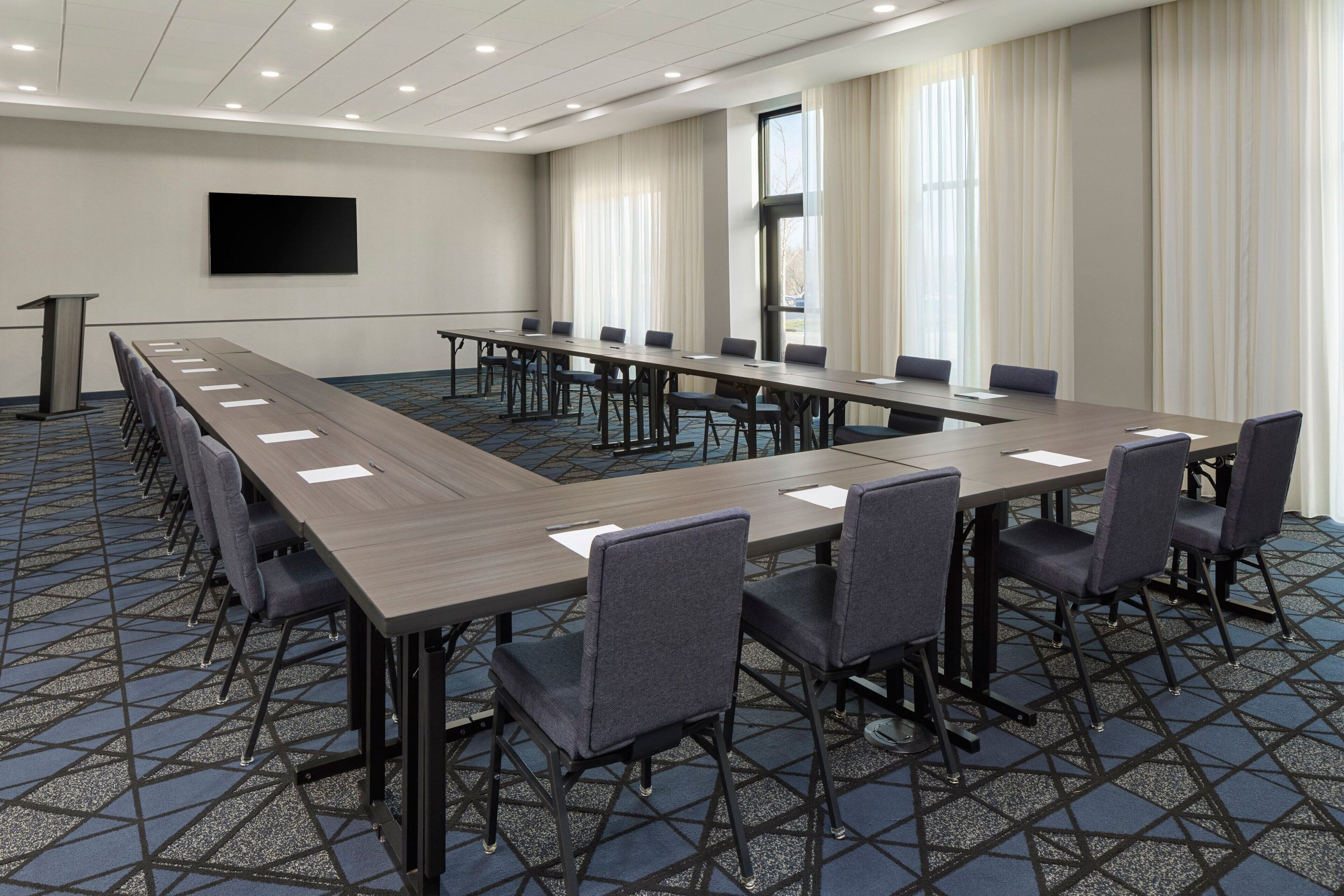 A conference room with a long table, chairs, a podium, and a large screen.