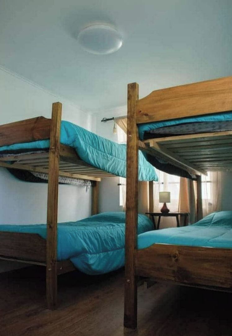 Een slaapkamer met stapelbedden, houten frames en blauwgroene beddengoed.