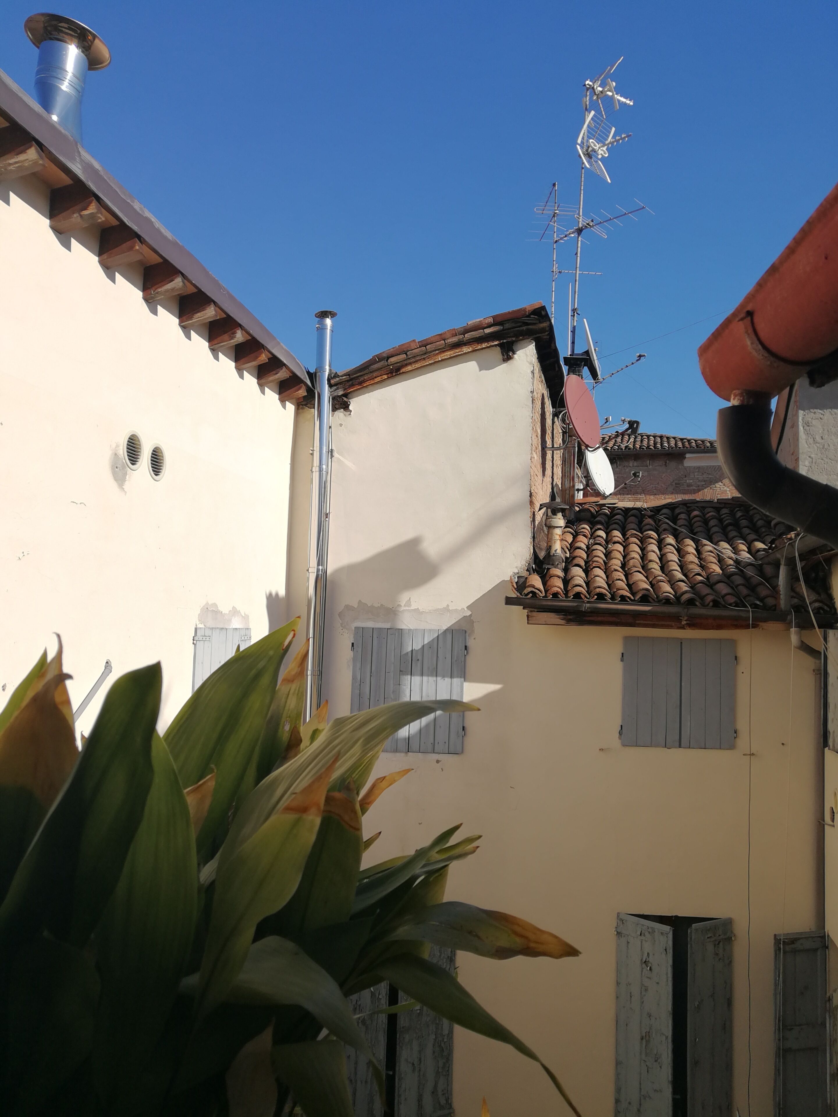 A building with a white facade, a chimney, satellite dishes, and a tiled roof.