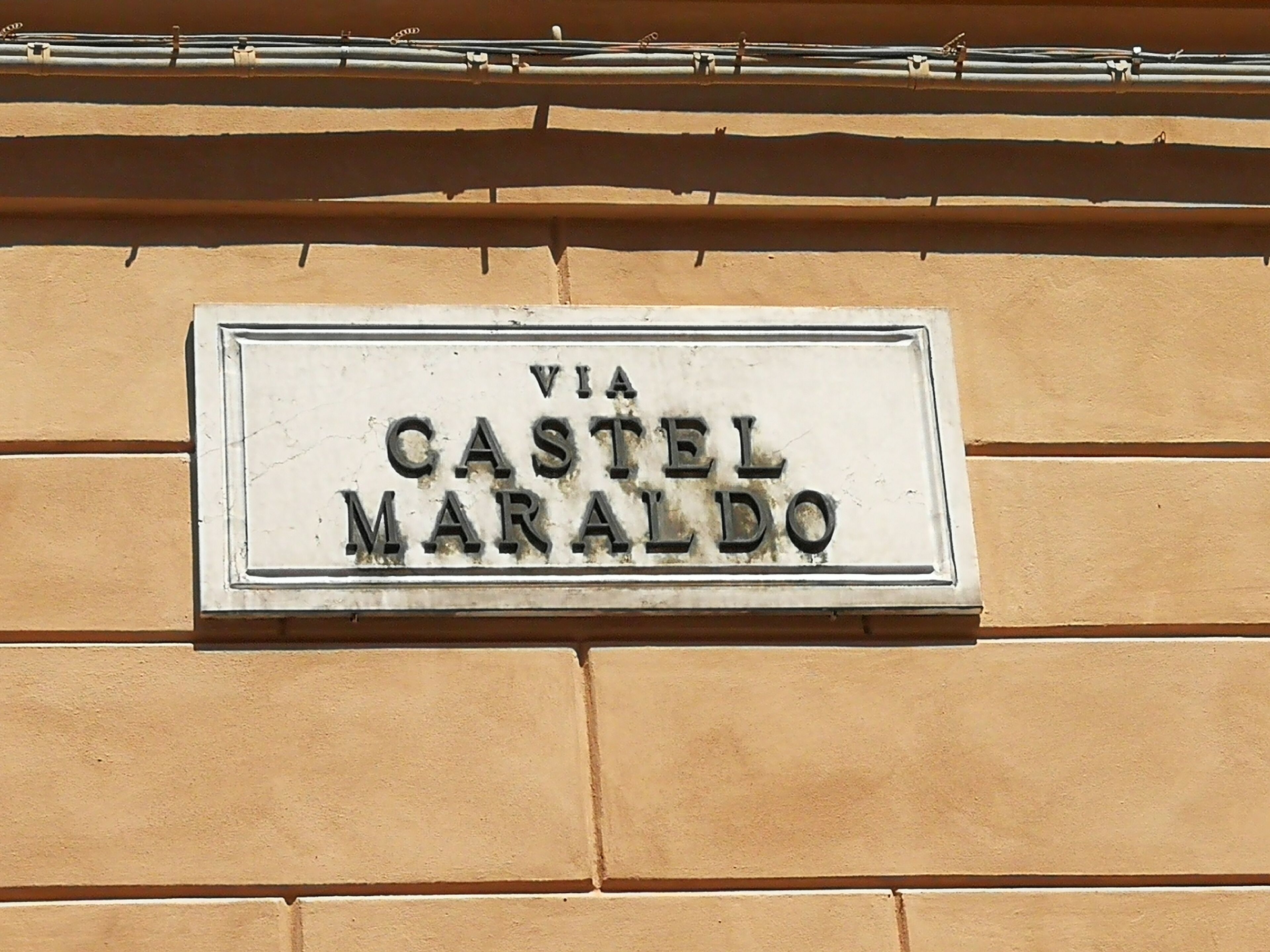 A sign on a building wall that reads 'VIA CASTEL MARALDO.'