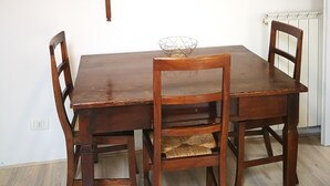 A wooden dining table with four chairs, a shelf above holding decorative items and books, and a radiator on the wall. - CA POMPOSA bed & relax  (Modena)