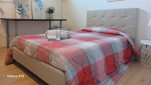A neatly made bed with a checkered bedspread, a bedside table with a lamp, and a framed picture on the wall. - CA POMPOSA bed & relax  (Modena)