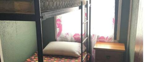 Habitación con literas, un pequeño armario de madera y una ventana con cortinas.
