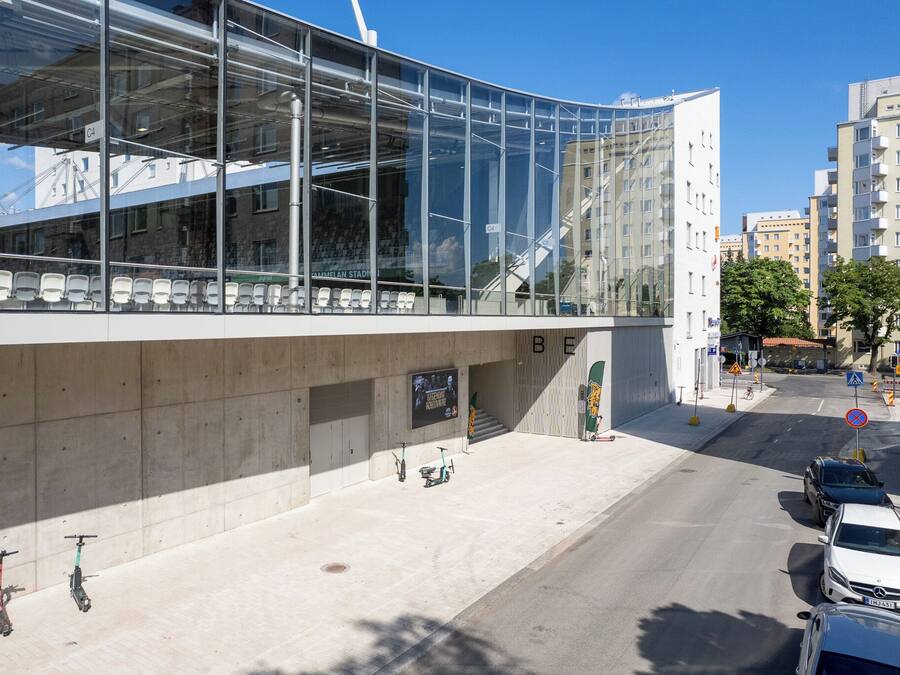 A modern building with large glass windows, a concrete facade, and a pedestrian area with parked scooters and cars.