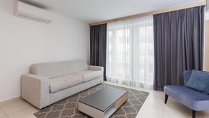 Una sala de estar moderna con un sofá gris, un sofá azul, una mesa de centro y un ventanal con cortinas.