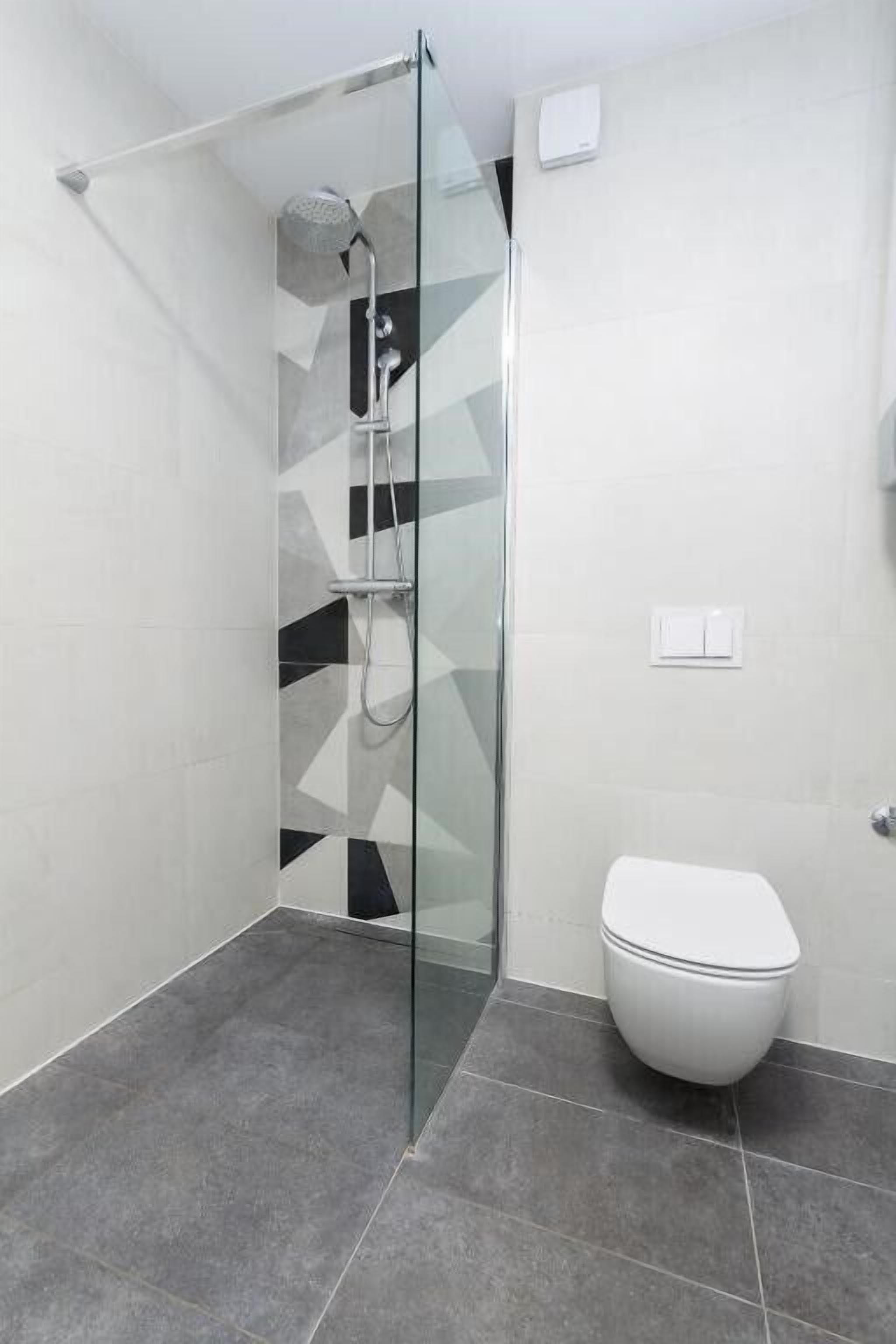 A modern bathroom with a glass-enclosed shower, a white toilet, and a geometric tile pattern on the walls.