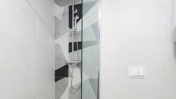 A modern bathroom with a glass-enclosed shower, a white toilet, and a geometric tile pattern on the walls.