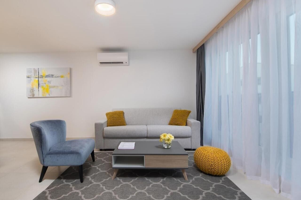 A modern living room with a grey sofa, a blue armchair, and a coffee table with a vase of flowers.