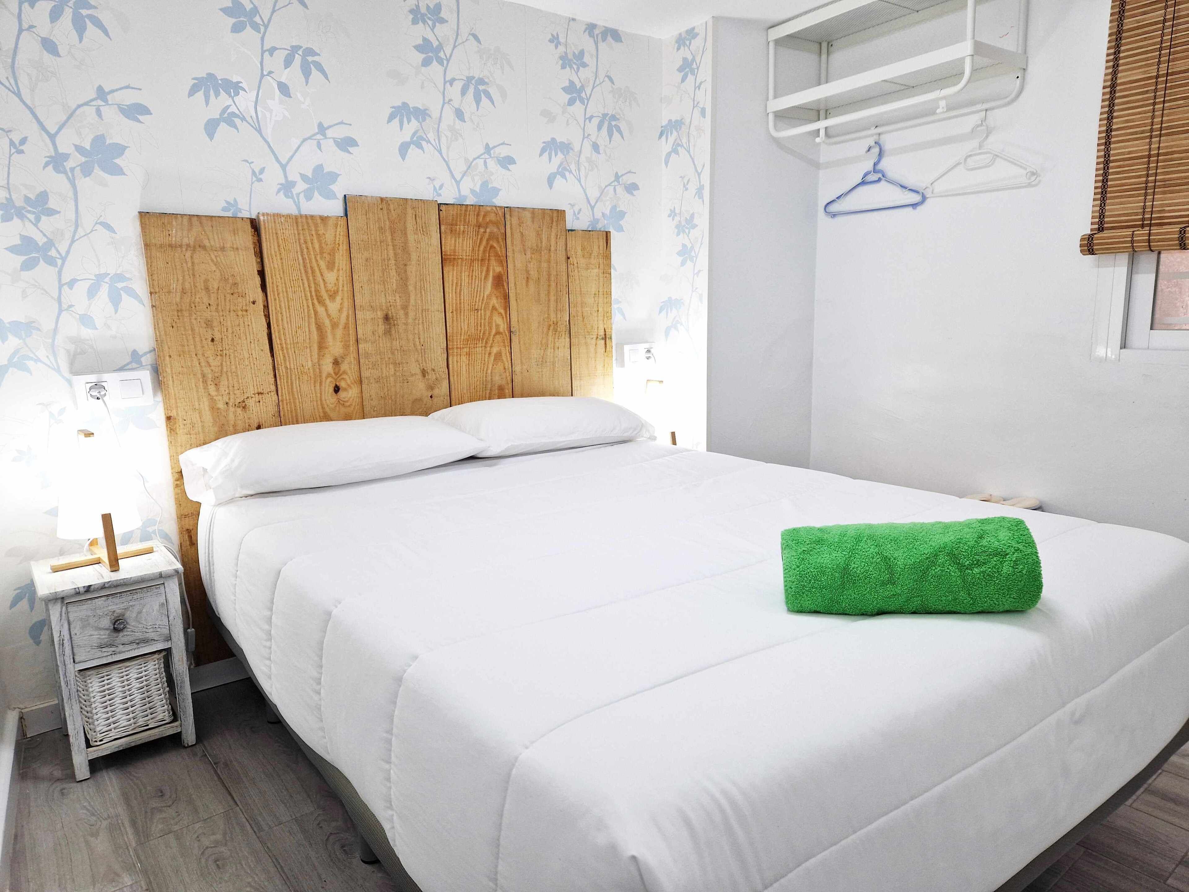 Una cama bien hecha con cabecera de madera, una mesita de noche con una cesta y una toalla verde sobre la cama.