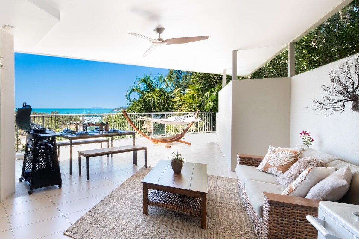 A balcony with a view of the sea, a hammock, a grill, and a sofa.