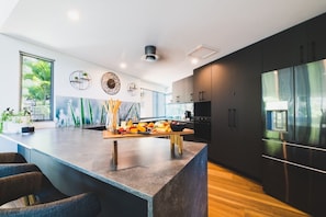 A modern kitchen with a large island, dark cabinetry, and a stainless steel refrigerator.