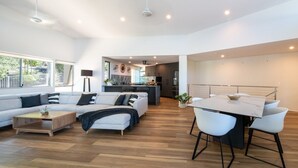 A modern living room with a sofa, coffee table, and dining area with chairs. - Picture Perfect On Azure (Airlie Beach)