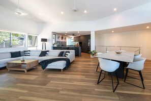 A modern living room with a sofa, coffee table, and dining area with chairs. - Picture Perfect On Azure (Airlie Beach)