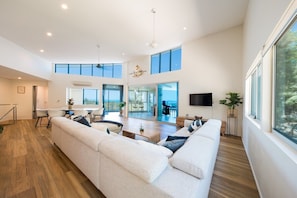 A spacious living area with a large sofa, dining table, and a view of the outdoors. - Picture Perfect On Azure (Airlie Beach)