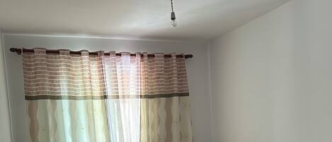 Quarto com duas camas de solteiro, piso de madeira e janela com cortinas leves.