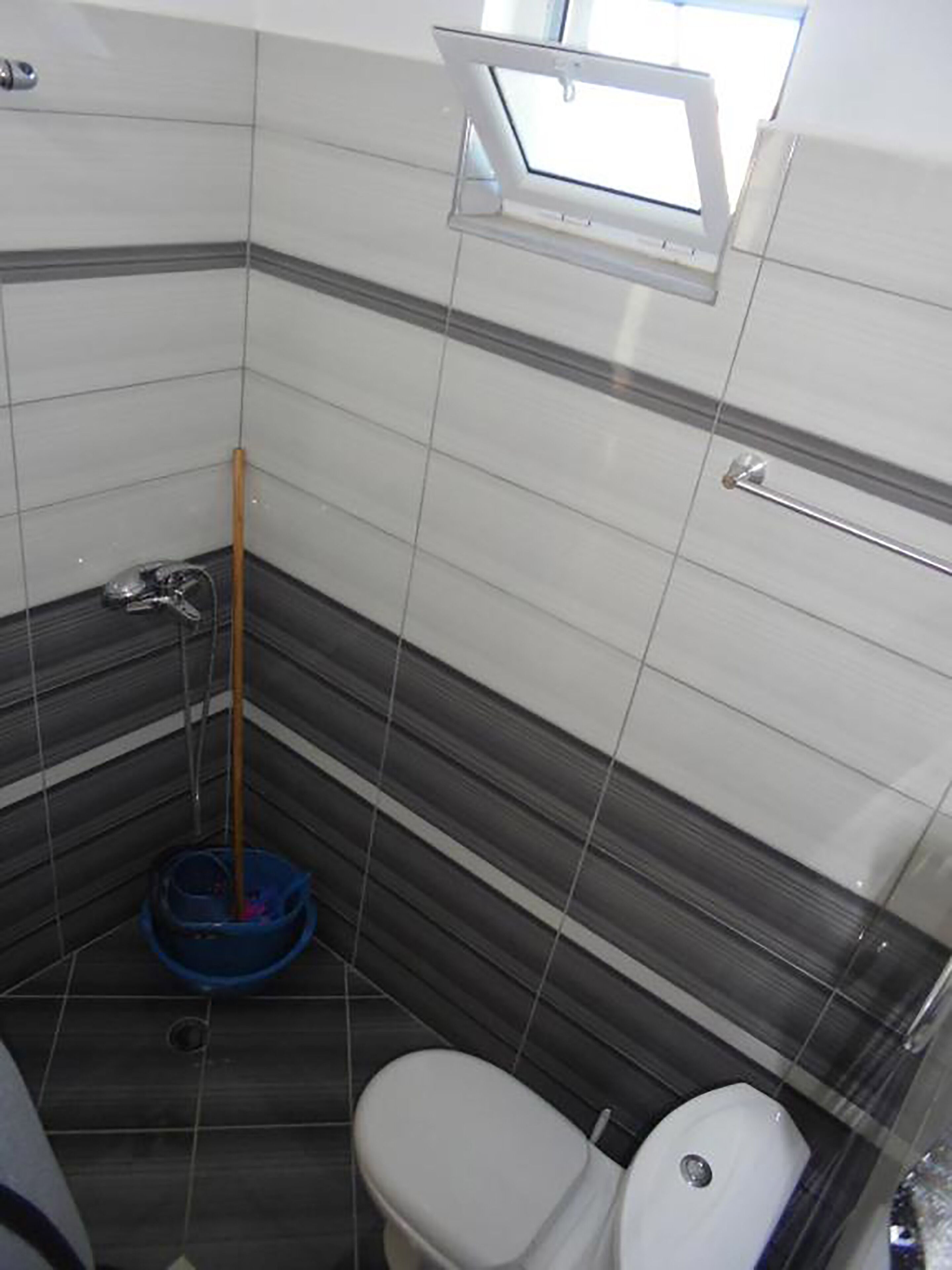 Ein Badezimmer mit Toilette, einem Mop und einem Fenster.