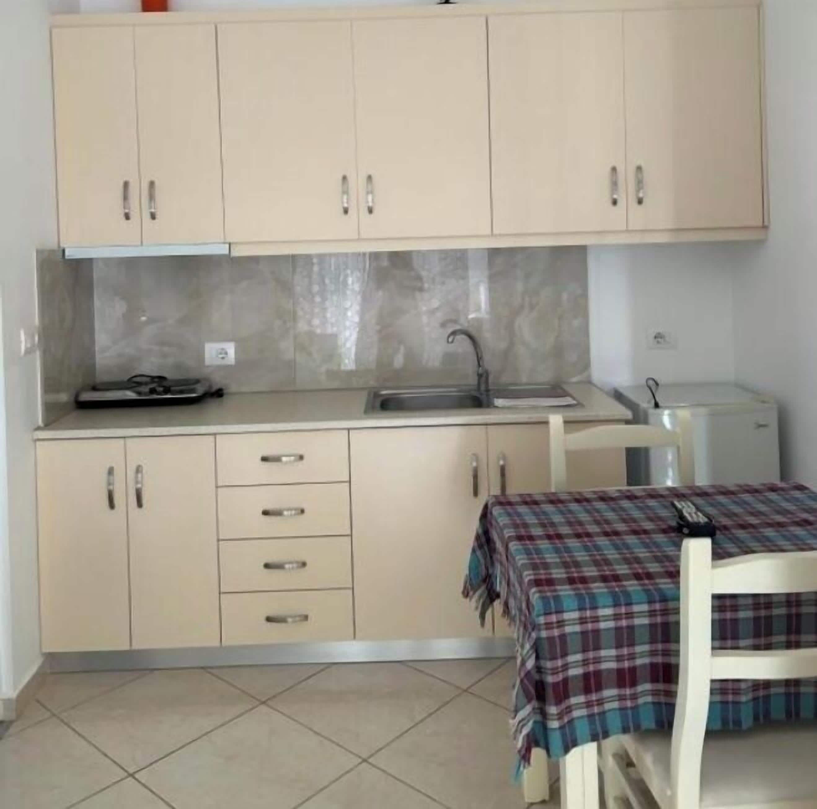 A small kitchen with beige cabinets, a sink, and a table with a plaid tablecloth.
