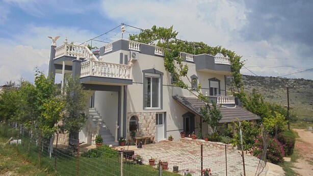 A two-story house with a balcony, stone steps, and a garden.