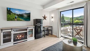 A modern living room with a fireplace, a television, a star decoration, and a balcony with outdoor seating. - The Southwestern Park City Mountain Resort Condo (Park City)