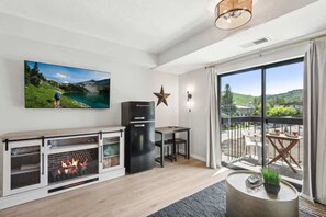 A modern living room with a fireplace, a television, a star decoration, and a balcony with outdoor seating. - The Southwestern Park City Mountain Resort Condo (Park City)